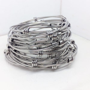 May include: A stack of silver bangle bracelets with a twisted wire design. The bracelets are stacked on top of each other, creating a layered effect.