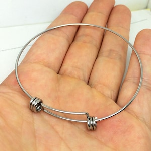 May include: A silver bangle bracelet with a spring clasp. The bracelet is made of thin metal and has a simple design.