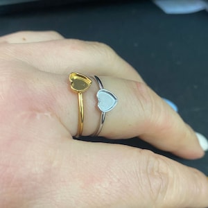 May include: Two heart-shaped rings, one gold and one silver, are worn on a finger. The rings are simple and elegant, with a smooth finish.