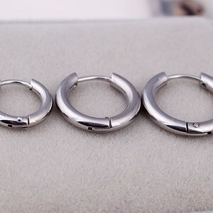 May include: Three silver hoop earrings of different sizes. The earrings are simple and minimalist in design.