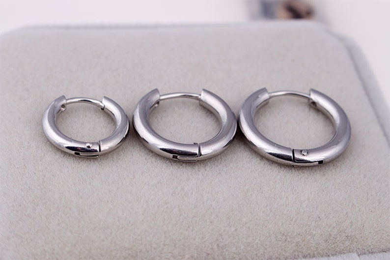 May include: Three silver hoop earrings of different sizes. The earrings are simple and minimalist in design.