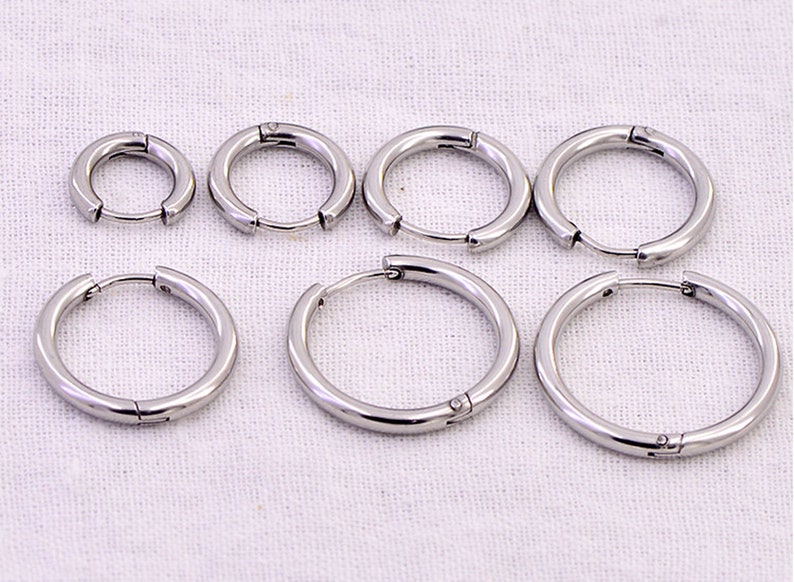 May include: Six silver hoop earrings of different sizes. The earrings are made of metal and have a hinged clasp.