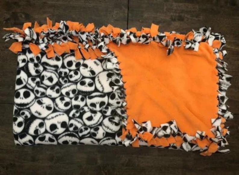 May include: A handmade fleece tie blanket with a black and white Jack Skellington print on one side and a solid orange fleece on the other side. The blanket has a knotted fringe border.