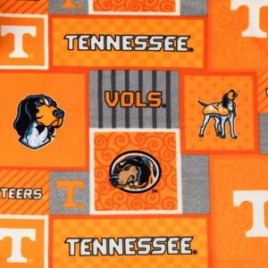 May include: Orange and gray fabric featuring the word "Tennessee" and the letter "T" in white. The fabric also displays images of a dog and the word "Vols".