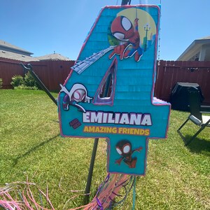 Może przedstawiać: Niebieska i r&oacute;żowa pi&ntilde;ata w kształcie cyfry 4, ozdobiona postaciami Spidermana. Pi&ntilde;ata ma napis "EMILIANA AMAZING FRIENDS".