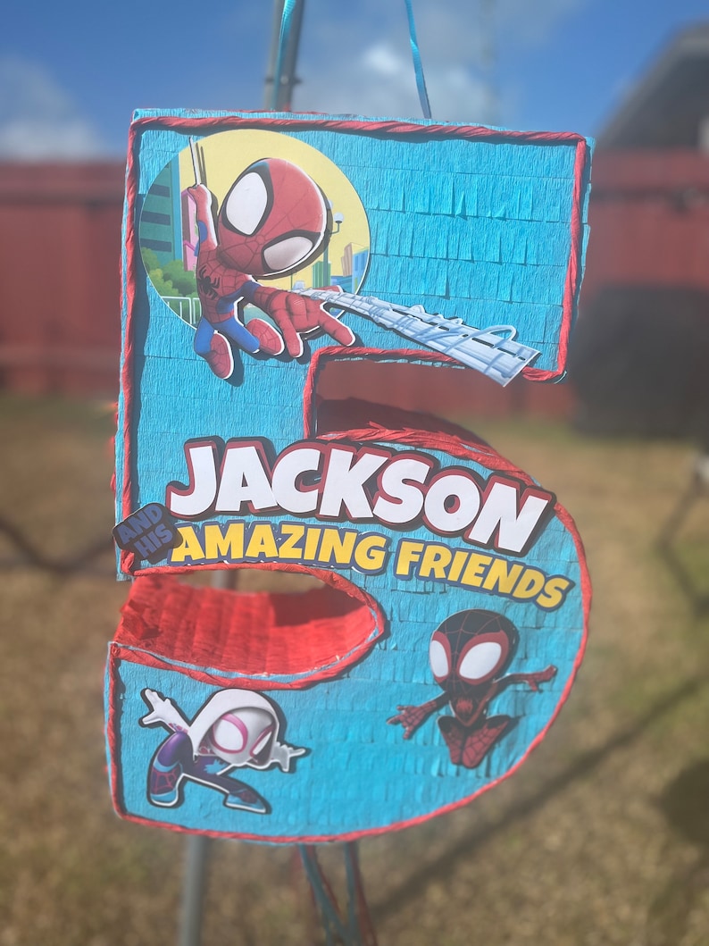 Może przedstawiać: Niebieska i czerwona pi&ntilde;ata w kształcie cyfry 5. Na g&oacute;rze znajduje się postać Spidermana, a na dole dwie inne postacie Spidermana. Pi&ntilde;ata ma napis "Jackson and his Amazing Friends".