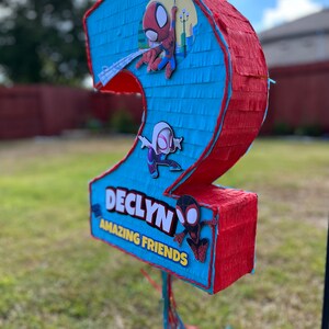 Może przedstawiać: Niebieska i czerwona pi&ntilde;ata w kształcie liczby dwa z motywem Spidermana. Pi&ntilde;ata ma napis "Declyn" i słowa "Amazing Friends".