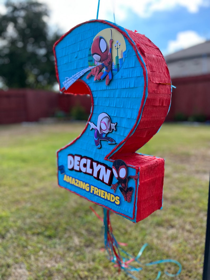 Może przedstawiać: Niebieska i czerwona pi&ntilde;ata w kształcie liczby dwa z motywem Spidermana. Pi&ntilde;ata ma napis "Declyn" i słowa "Amazing Friends".