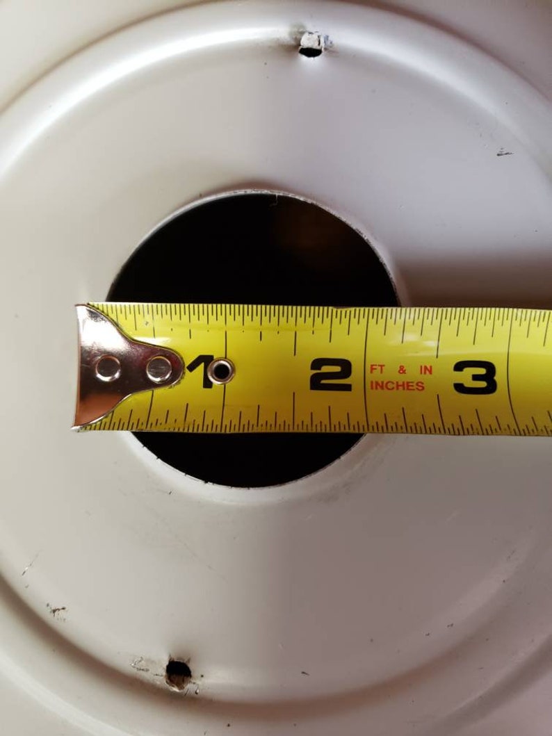 K&ouml;nnte beinhalten: Ein gelbes Ma&szlig;band mit schwarzen Markierungen liegt auf einem wei&szlig;en runden Objekt. Das Band zeigt "1", "2 FT & IN INCHES" und "3" an.
