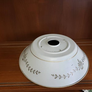 K&ouml;nnte beinhalten: Wei&szlig;er Lampenschirm aus Metall mit goldener Einfassung und floralem Muster. Der Lampenschirm hat in der Mitte ein Loch f&uuml;r eine Gl&uuml;hbirne.