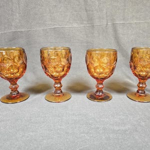 May include: A set of four amber-colored glass goblets featuring a raised circular dot pattern on the bowl. Each goblet has a short, thick stem and a circular base, crafted from translucent orange-toned glass with a consistent textured design.
