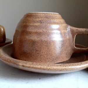 May include: A brown ceramic coffee cup and saucer set. The cup has a rounded shape and a speckled brown glaze. The saucer is a simple round shape.