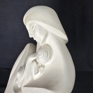 May include: A smooth, off-white speckled sculpture depicting a stylized figure cradling a smaller figure. The sculpture features clean, curved lines and a matte finish, showing a side profile of the larger figure looking down at the smaller one.