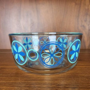 May include: A clear glass bowl with a blue and turquoise floral pattern. The bowl is round and has a smooth rim.