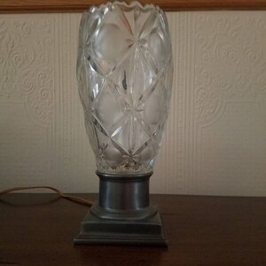 May include: A crystal lamp with a cut glass design and a pewter base. The lamp has a clear glass shade and a silver cord.