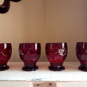 May include: Four red glass tumblers with a textured, bubbled design. The glasses have a wide base and a rounded top.