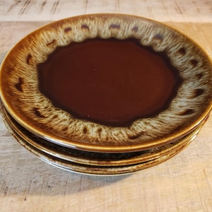 May include: A stack of three ceramic plates. The plates have a dark brown center with a lighter brown and cream-colored rim. The plates are stacked on top of each other, with the top plate in focus.