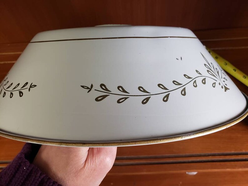 K&ouml;nnte beinhalten: Ein wei&szlig;er Lampenschirm aus Metall mit goldener Einfassung und braunem Blattdesign.