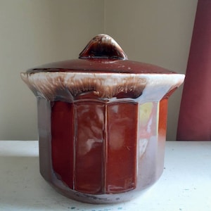 May include: A brown and white glazed ceramic cookie jar with a lid. The jar has a rounded, octagonal shape and a smooth, glossy finish.