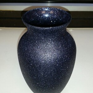 May include: A navy blue vase with a glittery, textured surface. The vase has a rounded body and a flared rim. The glitter catches the light, creating a sparkling effect. This decorative vase is suitable for displaying flowers or as a standalone accent piece.