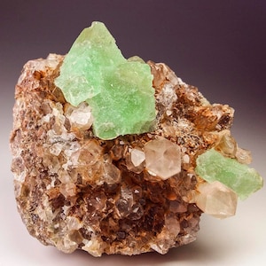 May include: A cluster of green fluorite crystals on a matrix of smoky quartz crystals. The fluorite crystals are translucent and have a glassy lustre. The quartz crystals are clear and have a slightly milky appearance.