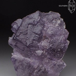 May include: A cluster of purple fluorite crystals with a cubic habit. The crystals are translucent and have a glassy luster. The fluorite is mounted on a gray base.