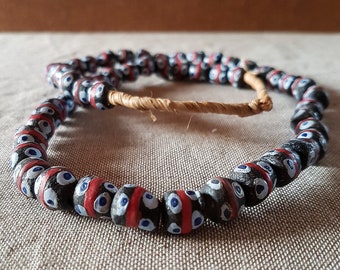 May include: A necklace made of black glass beads with white and red painted details. The beads are round and have a pattern of small white circles and a red stripe around the middle.