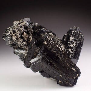 May include: A cluster of black schorl crystals with a glassy luster. The crystals are intergrown and have a rough, textured surface.