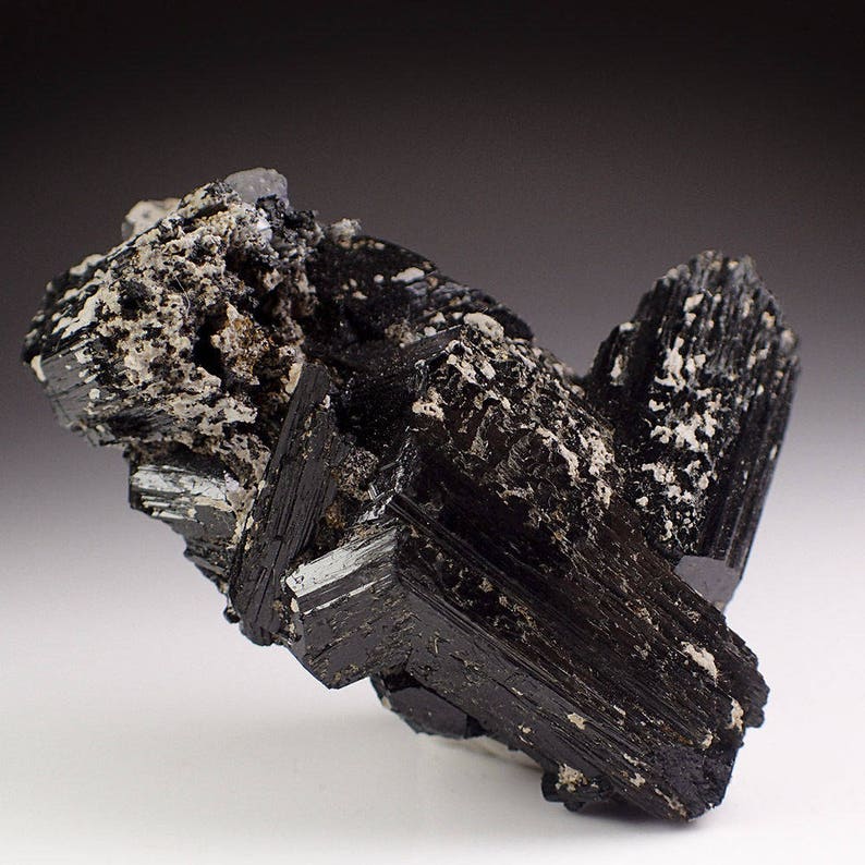 May include: A cluster of black schorl crystals with a glassy luster. The crystals are intergrown and have a rough, textured surface.