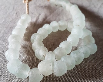 May include: A strand of white glass beads with a frosted finish. The beads are strung on a natural fiber cord.