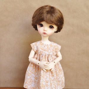 May include: A porcelain doll with brown hair wearing a white dress with a brown floral pattern.