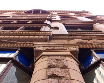 May include: A low angle view of a building with a brick facade and ornate detailing. The building has many windows and a large column in the foreground.