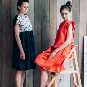 Peut inclure: Deux femmes portant des robes, l'une en robe bleu marine avec un motif blanc et noir, l'autre en robe rouge. La femme en robe rouge est assise sur un tabouret en bois.