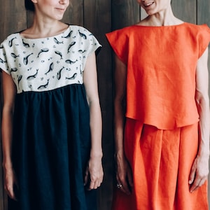 Peut inclure: Deux femmes portant des robes en lin. La femme de gauche porte une robe blanche &agrave; imprim&eacute; baleine et une jupe bleu marine. La femme de droite porte une robe orange unie.