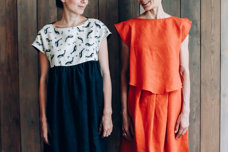 Peut inclure: Deux femmes portant des robes en lin. La femme de gauche porte une robe blanche &agrave; imprim&eacute; baleine et une jupe bleu marine. La femme de droite porte une robe orange unie.