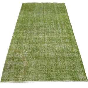 May include: A green vintage rug with a distressed look. The rug has a subtle pattern and a white fringe border.