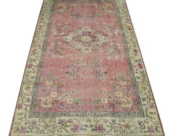 May include: A vintage rug with a pink background and a floral pattern. The rug has a cream-coloured border with a floral design.