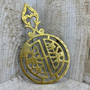 May include: A brass trivet with an intricate design. The trivet is round with a decorative handle. The design features a repeating pattern of leaves and flowers.