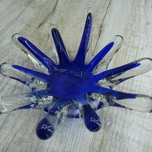 Könnte beinhalten: Eine blaue Glasschale mit einem Sternburst-Design. Die Schale hat einen klaren Glasboden und blaue Glasarme, die sich vom Zentrum aus erstrecken. Die Schale ist perfekt, um kleine Gegenstände wie Schmuck oder Schlüssel aufzubewahren.