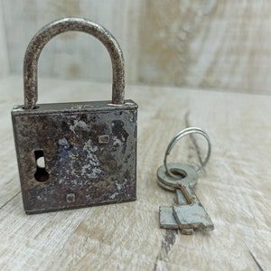 May include: A rusty metal padlock with a keyhole and a matching key. The padlock is closed and has a worn, aged appearance.