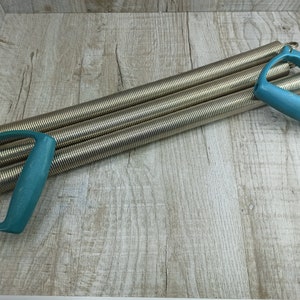 May include: A silver exercise expander with two teal plastic handles. The expander is made of multiple coiled springs.