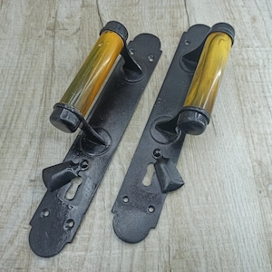 May include: Two black door handles with yellow plastic handles. The handles have a keyhole and a decorative design.