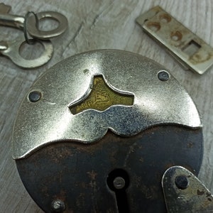 May include: A vintage padlock with a silver-colored body and a black metal handle. The padlock has a keyhole and a brass-colored plate with the inscription "S.I.P. 15".