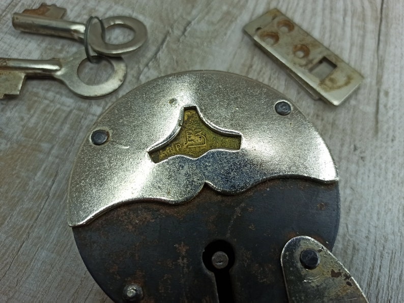 May include: A vintage padlock with a silver-colored body and a black metal handle. The padlock has a keyhole and a brass-colored plate with the inscription "S.I.P. 15".