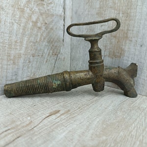 Può includere: Un rubinetto in ottone antico con un beccuccio filettato e una maniglia con un anello. Il rubinetto ha una patina usurata e invecchiata.