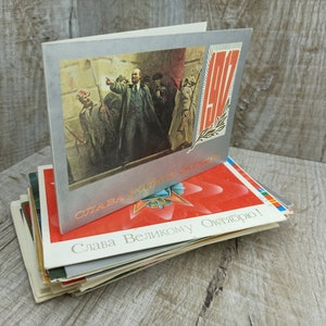 May include: A stack of vintage postcards featuring Soviet-era imagery. The top card has a silver border and a painting of a man addressing a crowd. Other cards display red stars and Cyrillic text.