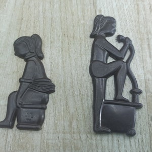 May include: Two black silhouette figures of people on a wooden surface. The figure on the left is sitting on a toilet. The figure on the right is sitting on a toilet and holding a shower head.