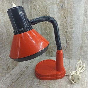 May include: A red and black desk lamp with a flexible arm and a black cord. The lamp has a red base and a red shade.