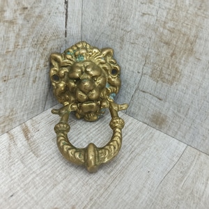 May include: A brass door knocker with a lion's head design. The knocker has a ring handle and is in a worn, antique style.