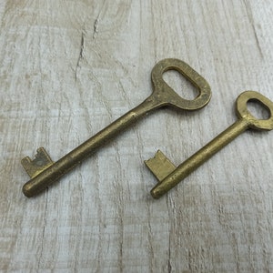 May include: Two antique brass keys, one with a simple round head and the other with a more ornate, rectangular head. Both keys have a worn, aged look.